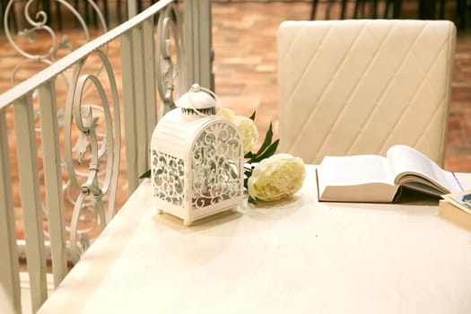 There is a beautiful table that features a lantern, vibrant flowers, and an interesting book resting upon it, creating a lovely scene