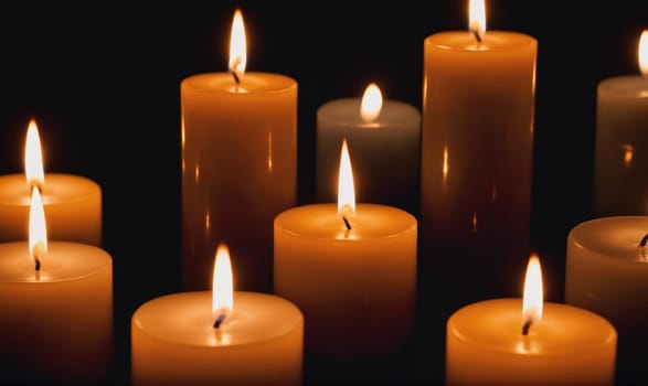 Multiple lit candles are arranged in a cluster against a black background, with the orange flames flickering and casting soft reflections.