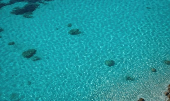 A view of the ocean from above, showing clear turquoise water with some rocks and small waves.
