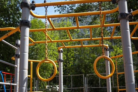 child hanging from a playground structure yellow metal ones. Outdoor sports activities.