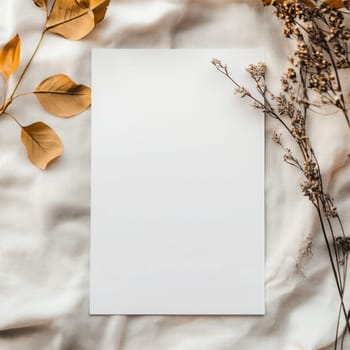 A piece of blank paper lies on a textured fabric backdrop surrounded by delicate dried flowers, creating an inviting space for writing or artistic projects.
