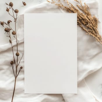 A piece of blank paper lies on a textured fabric backdrop surrounded by delicate dried flowers, creating an inviting space for writing or artistic projects.