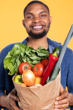Cheerful person advocates for sustainable vegan lifestyle in studio, carrying a paper bag of fresh organic groceries. Eco friendly guy shopping to promote zero waste and delicious produce.