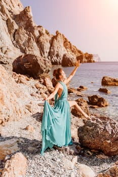 Woman green dress sea. Woman in a long mint dress posing on a beach with rocks on sunny day. Girl on the nature on blue sky background