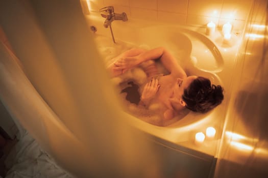 Woman lying in bath foam at bathroom. Romantic girl relaxing at bathtub at home. Close up sexy woman taking bath indoors