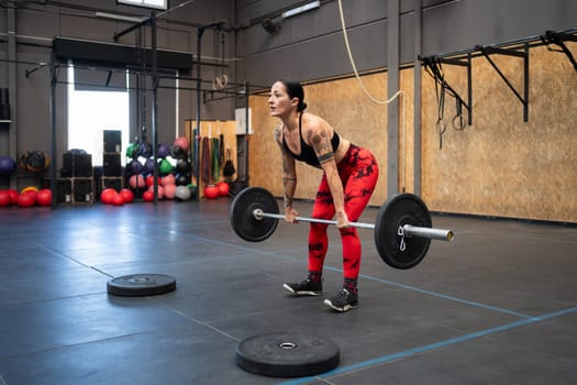 Fit mature woman dead-lifting alone with a bar and weights in a cross training center