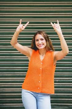 Vertical photo of a latin woman smiling doing the heavy metal horns hand sign