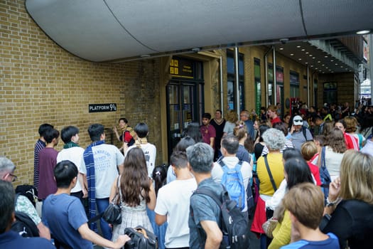 London, UK, july 20th 2024. Japanese young people pretending to hold a wand as people queue for a photo with the Harry Potter trolley on the imaginary platform 9 3-4 at King's Cross station.