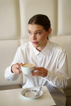Vertical photo of a distracted elegant woman holding coffee cup in a cafeteria