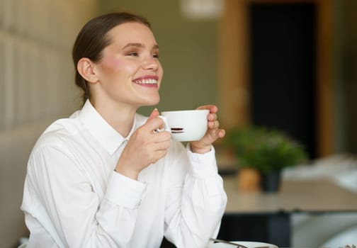 Smiling businesswoman enjoying a delicious aromatic coffee in a cafeteria sitting alone holding the mug