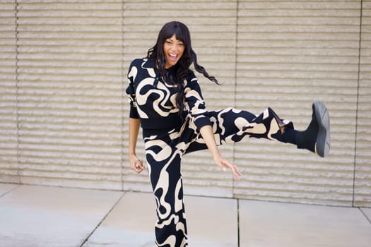 Energetic dancer laughing and raising the leg while performing outdoors in the city street