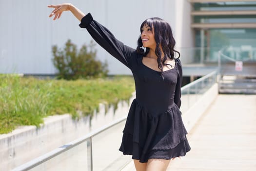 Vital woman raising hand while dancing under the sun in the city