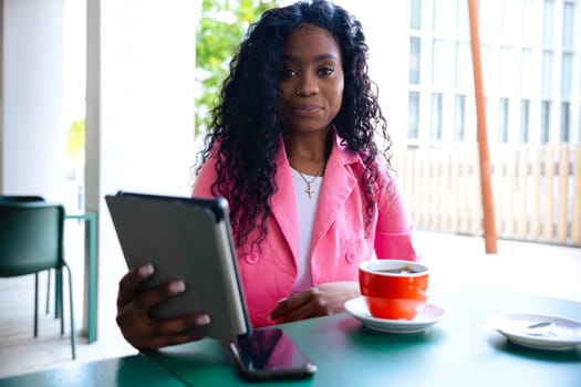 Beautiful black woman with curly hair using her smartphone to chat with friends looking at camera. connected concept