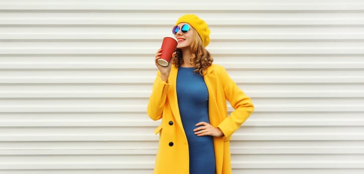 Autumn portrait of beautiful happy smiling young woman with cup of coffee drink in yellow french beret hat, coat jacket posing on white background
