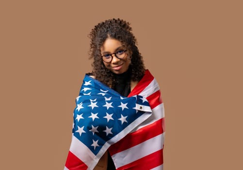Smiling african american woman with national USA flag on beige background. American patriot, 4th of July - Independence day celebration, election, America, labor. US banner. High quality