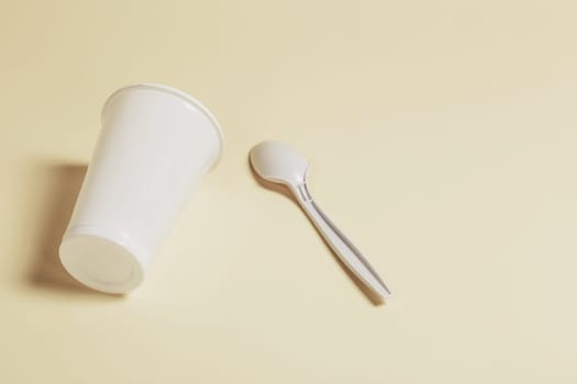 White plastic glass and spoon on a paper background.