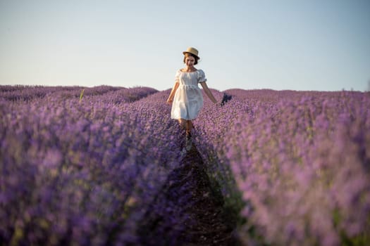 Lavender field happy girl in white dress with hat runs through a lilac field of lavender. Aromatherapy travel.