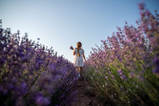 Lavender field girl. Back view happy girl in white dress with a scythe runs through a lilac field of lavender. Aromatherapy travel.