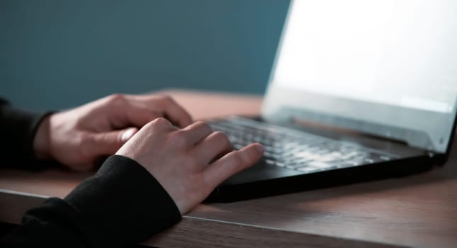 Male hands with a sun effect are typing on a laptop keyboard, close-up view. A man works in an office, is engaged in the development of his business at home, writes messages online.