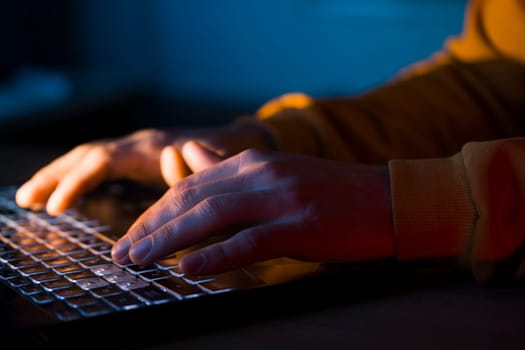 Male hands are typing on a laptop keyboard, a man works, develops a business, studies, plays a computer game at night. Close-up view.
