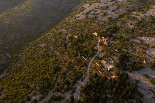 Aerial view of a serene village surrounded by lush greenery during sunset in a mountainous area.