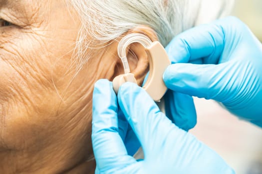 Asian senior woman patient wearing a hearing aid for treating hearing loss problem.