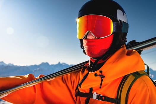 Portrait of a skier with skis on his shoulder. Guy on a background of a mountain range on a sunny winter day, sunlight, outdoor recreation, skiing, sports concept.