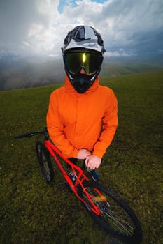 Portrait of a cyclist in a full-face helmet and sunglasses on the background of a mountain. Mountain biker, unrecognizable man on modern bike.