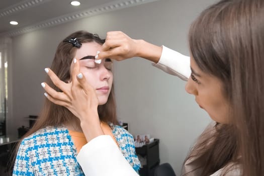Eyebrow tinting. Close-up of a master applying eyebrow paint with a brush, washing off excess paint from the eyebrows or skin. Cosmetic procedures, eyebrow makeup in a beauty salon.