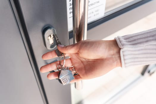 A woman's hand opens the door with a key on which the keychain hangs at home
