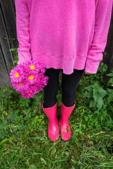 A woman in pink boots and a pink sweater holds a beautiful pink bouquet of flowers in her hands. The girl is standing in the street