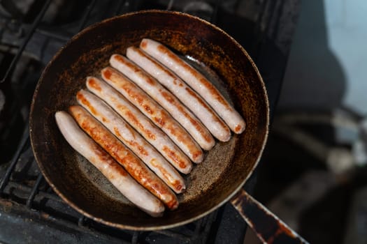 Baked thin long pork sausages in natural casing on the old cast frying pan on rustic table, top view