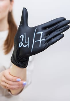 A woman's hand in a black rubber glove on which is written 24 7, help at any time, always in touch. Support and help concept