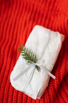 A homemade Christmas stollen sealed in white craft paper lies on a red knitted fabric. Gift wrap