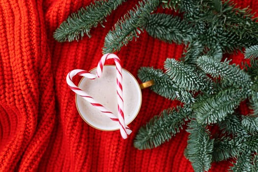 Christmas composition made of Norwegian Nobilis pine and decorated with lights and candy canes in the form of a cane. A cup of cappuccino with a candy cane in the shape of a heart. Christmas and New Year concept