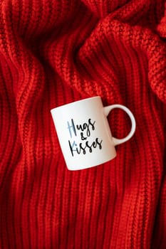 Hugs and kisses inscription on a white cup on a red knitted fabric. Love concept. St. Valentine's Day