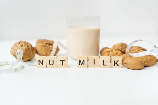 Vegan milk from nuts in a glass cup with various nuts on a white table. Lettering nut milk