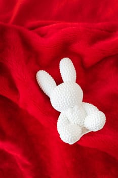 A red ceramic white rabbit lies on a red background. Symbol of the new year 2023. Concept of gifts and surprises, place for inscription