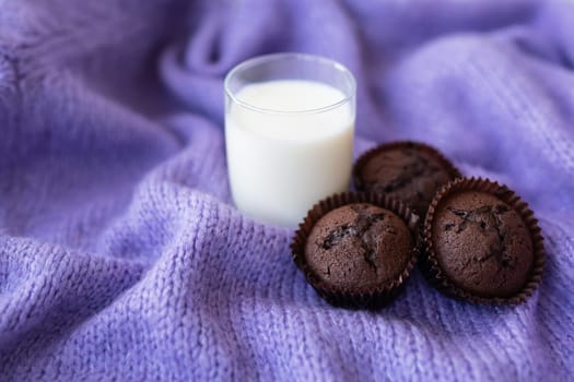 Chocolate cupcakes, along with a glass of milk, stand on a purple knitted fabric. Close-up, place for an inscription