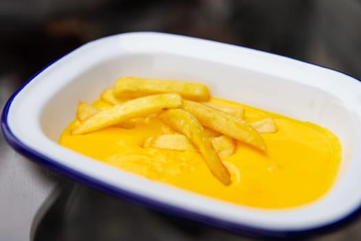 The concept of fast food and fast food. French fries sit in a plate along with cheddar cheese sauce. Top view, close-up