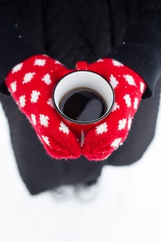 Hands in red gloves hold a mug of hot drink. Beautiful snowy winter, top view