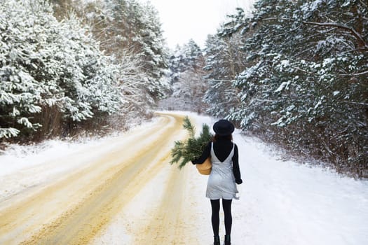 A girl in a dress and hat stands with her back in the middle of a winter road in the forest