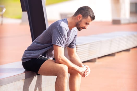 Portrait of a handsome, tired young man in sportswear looking down as he takes a break from his track and field training workout routine.