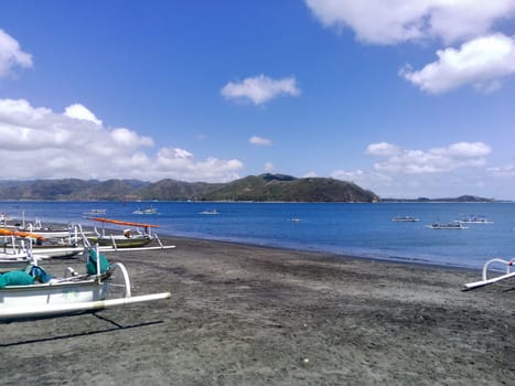 A serene beach near Cemare Beach, Lombok, Indonesia. Scene with a traditional fishing boat, clear blue sky, and gentle waves.