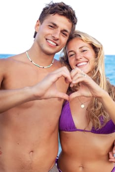 Portrait of happy couple on the beach building a heart with her hands with the sea in the background.Vertical