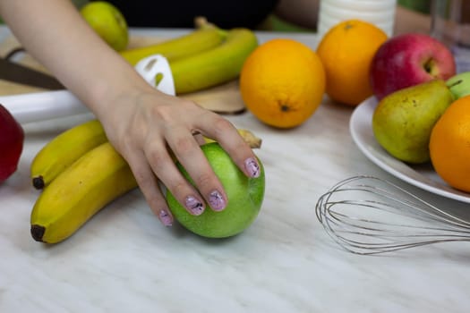 Woman hand takes apple to make healthy fruit juice drink. Sports cocktail with blender at home for boost vitamins
