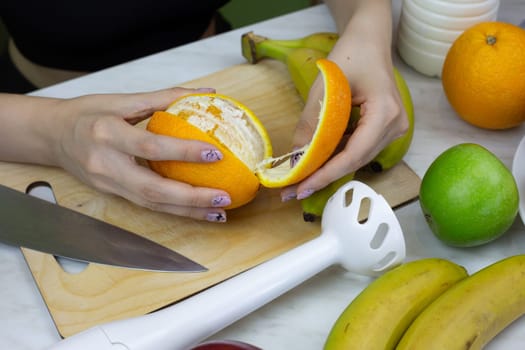 Girl peels ripe orange to make sports shake in blender, healthy eating and getting vitamins at home, sport eat concept