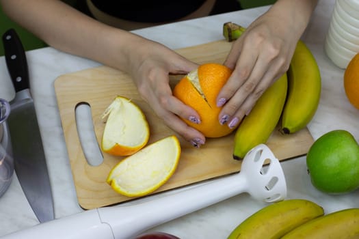 Girl peels an orange while making healthy drink in blender. Homemade sports fruit cocktail to improve health and boost vitamins