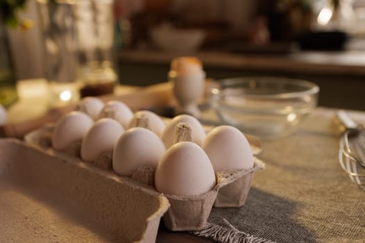 A close-up of a carton of white eggs on a kitchen countertop, with a blurred background showing a person and kitchen utensils