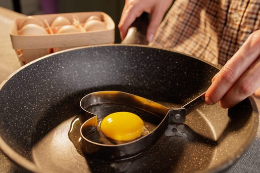 close-up of female hands holding a heart shape on a frying pan with a broken egg, heart-shaped fried egg